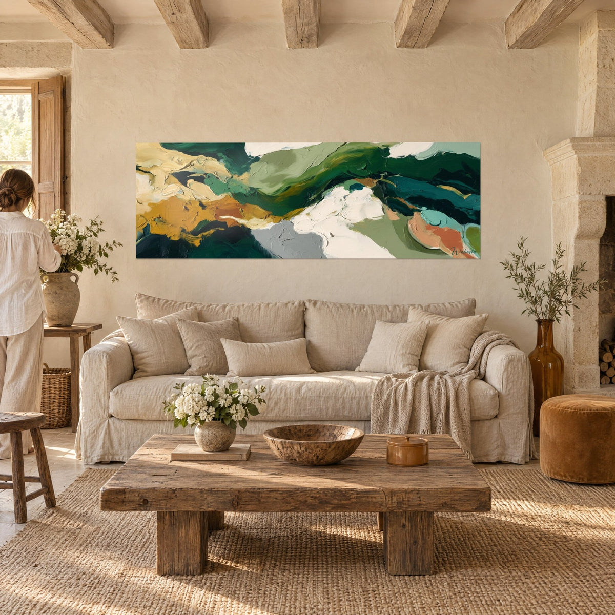 Wall art abstract landscape in fir green and golden ochre with thick flowing paint layers, person seen from behind, above a sofa in a bright living room