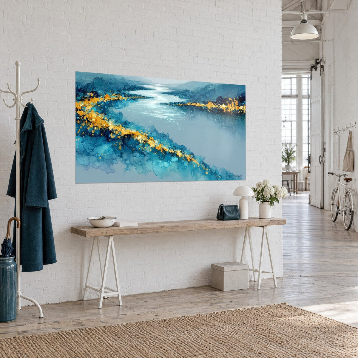 Tableau méandre d'eau argentée entre berges bleu profond et éclats d'or, sur un mur blanc près d'une console en bois
