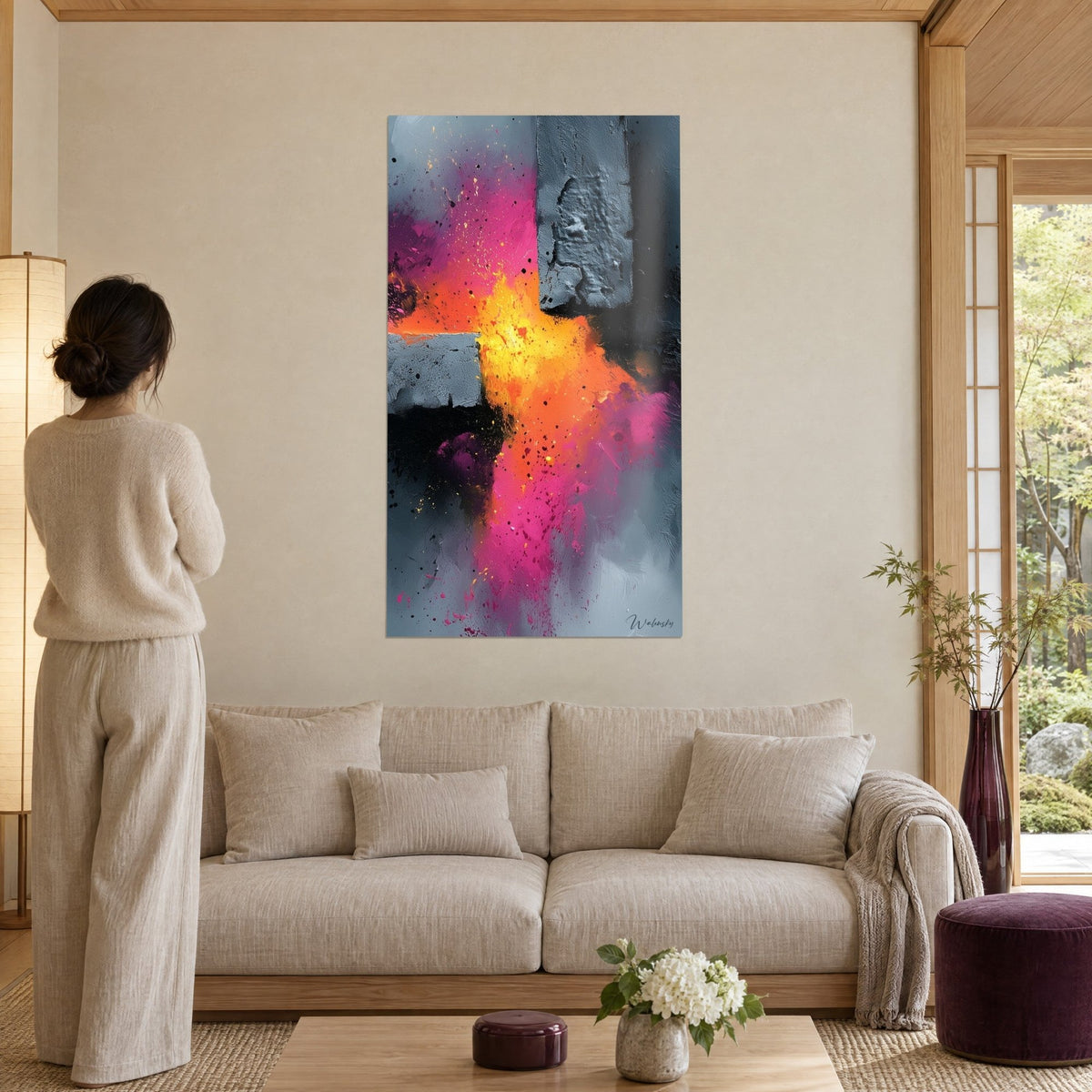Wall art powder explosion in pink and orange on charcoal grey, woman seen from behind above a sofa in a bright living room