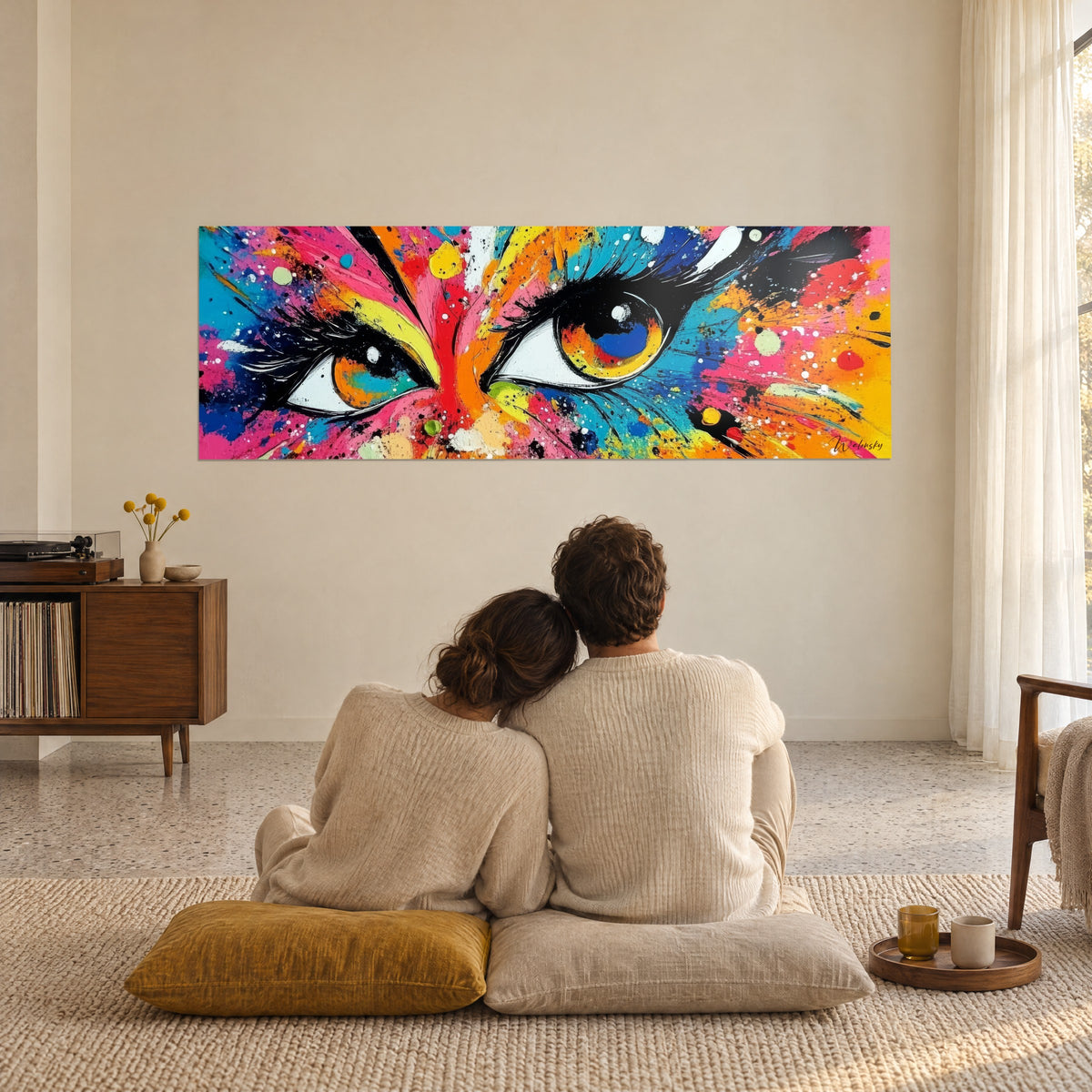 Cuadro de una pareja de espaldas sentada sobre cojines mostaza frente a una pared beige, pintado con gotas de pintura rosa, azul y amarilla vivas