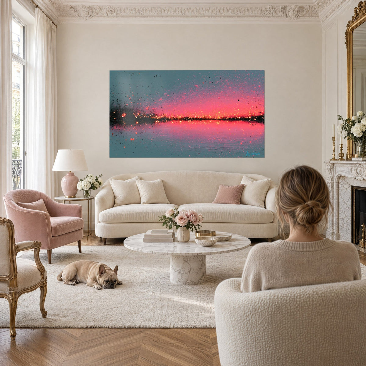 Cuadro horizonte incandescente en rosa coral sobre fondo gris azulado, destellos dorados, una mujer de espaldas, encima de un sofá en un salón luminoso