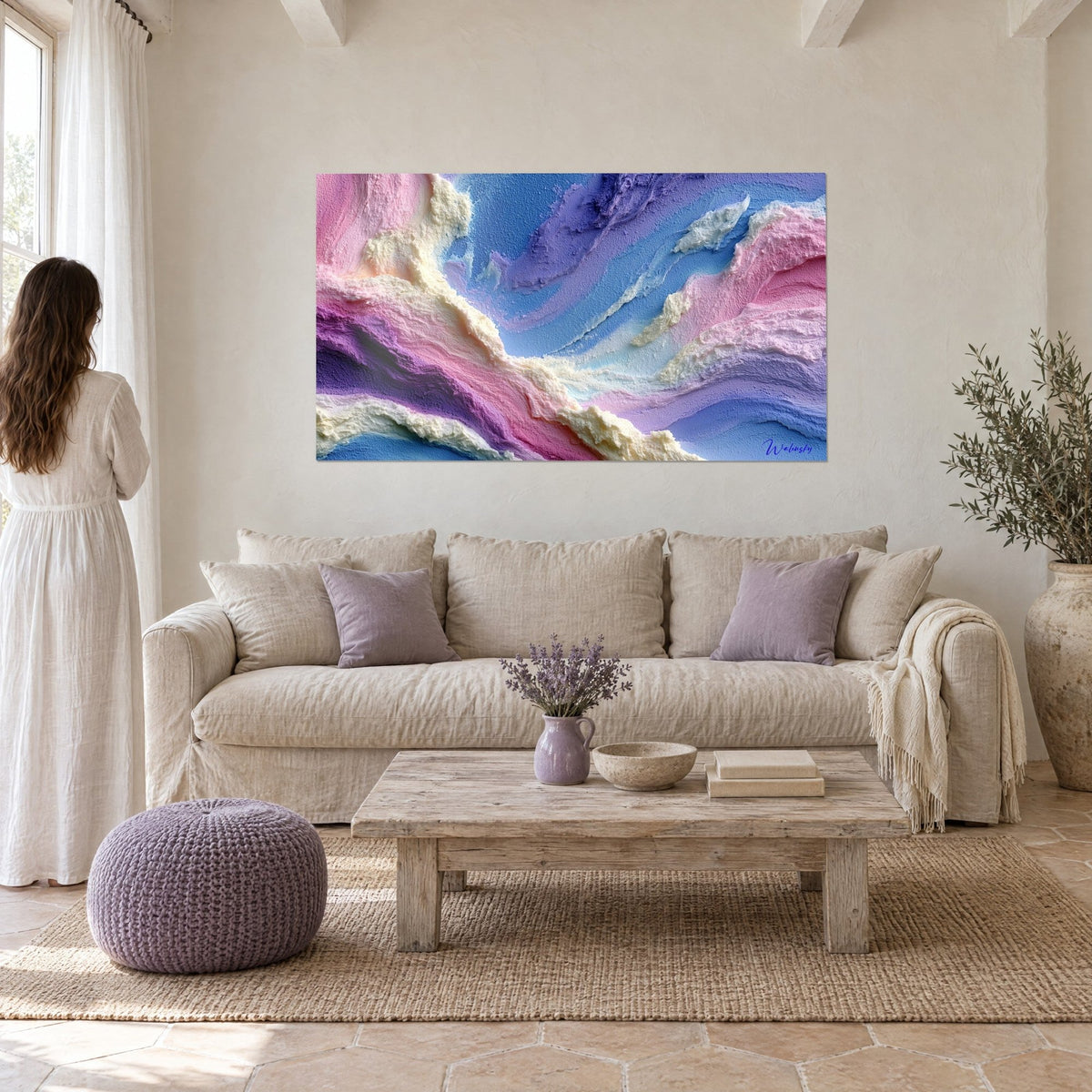 Tableau vagues crémeuses rose et bleu pastel en relief, femme de dos, au-dessus d'un canapé dans un salon lumineux