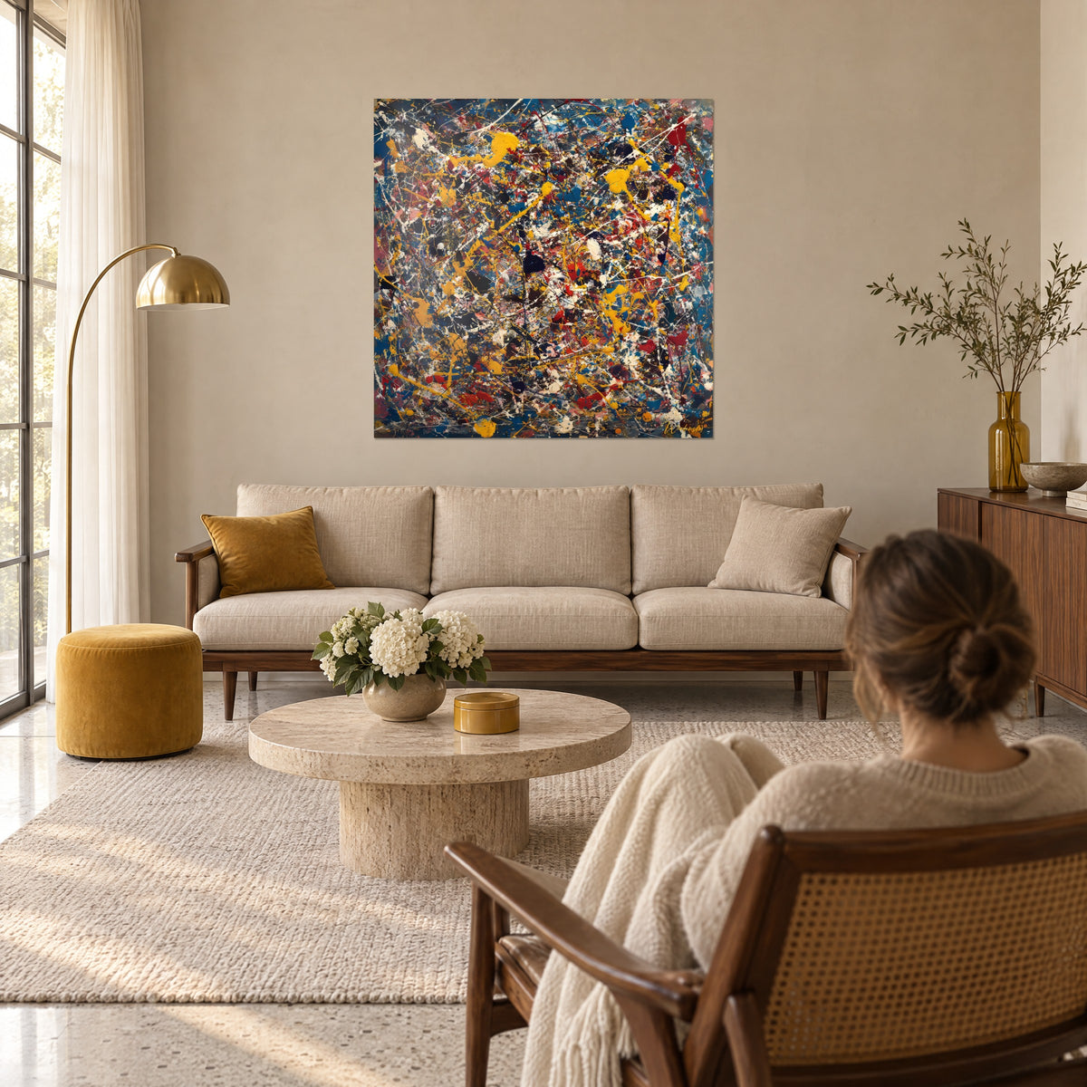 Cuadro salpicaduras amarillo mostaza y azul cobalto sobre fondo negro, chorreados blancos, mujer de espaldas, encima de un sofá en un salón luminoso