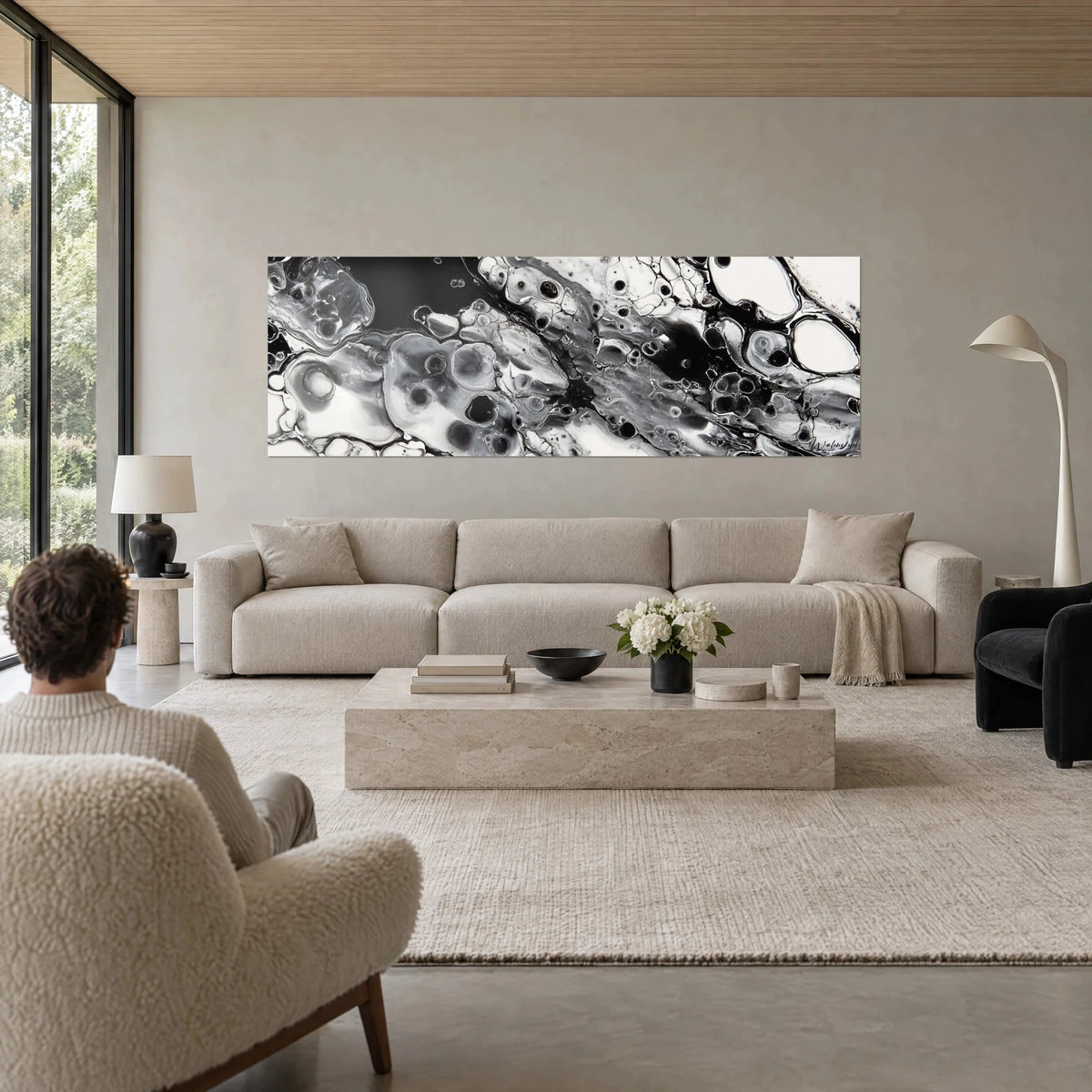 Wall art with black and white marbled fluid ink cells, silvery reflections, person seen from behind, above a sofa in a bright living room