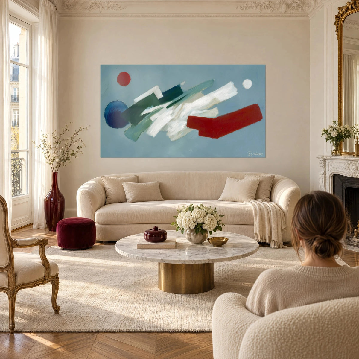 Tableau coups de pinceau géométriques blancs, verts et rouges sur fond bleu-gris, au-dessus d'un canapé dans un salon lumineux