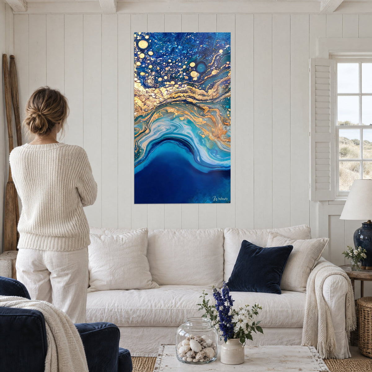 Tableau marbrure bleu nuit veinée d'or et bulles scintillantes, femme de dos au-dessus d'un canapé dans un salon lumineux