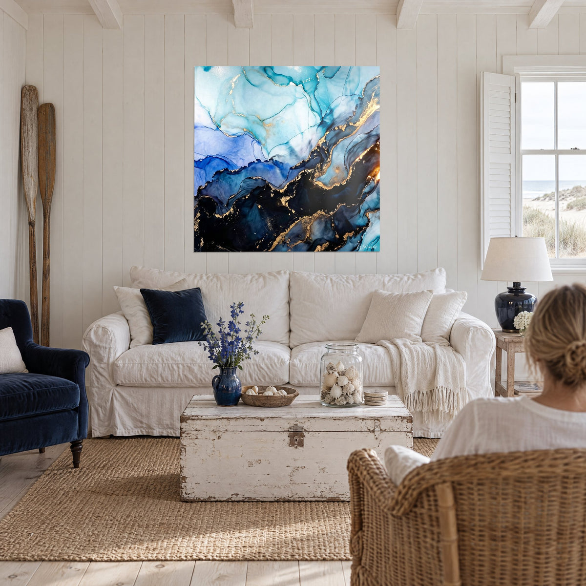 Tableau marbrure d'encre turquoise et noir veinée d'or, vue de dos, au-dessus d'un canapé dans un salon lumineux