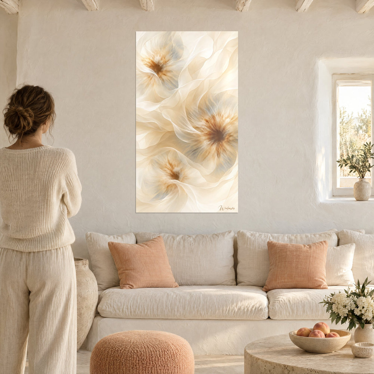 Tableau fleurs abstraites beige et ambre aux voiles translucides, vu par une femme de dos, au-dessus d'un canapé dans un salon lumineux
