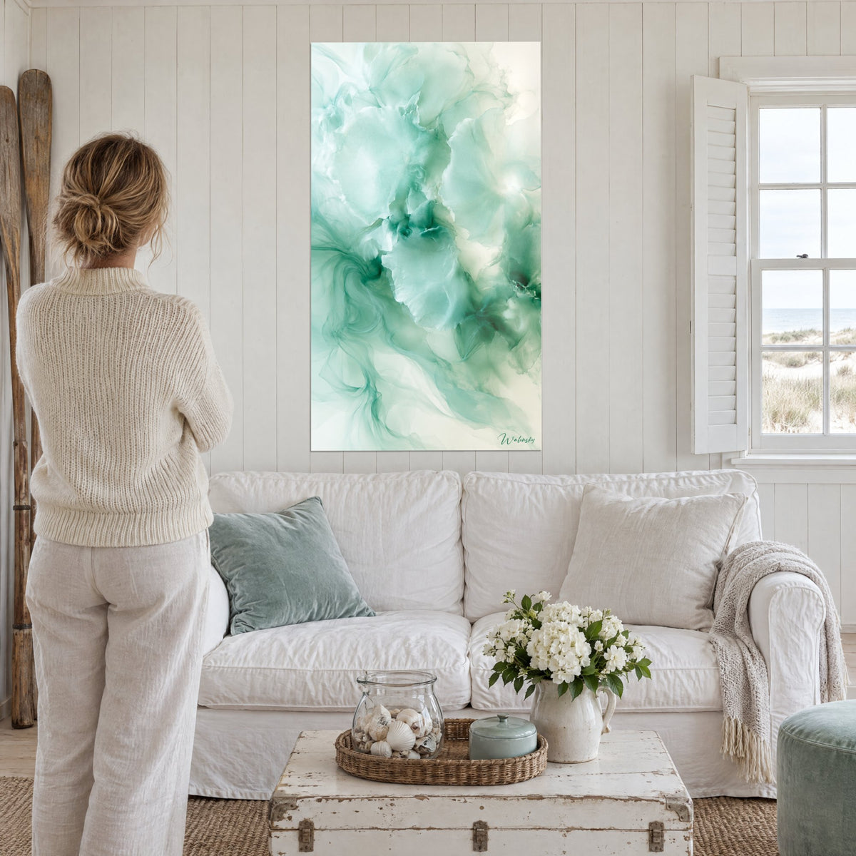 Tableau pétales d'encre céladon et blanc nacré, femme de dos devant, au-dessus d'un canapé dans un salon lumineux