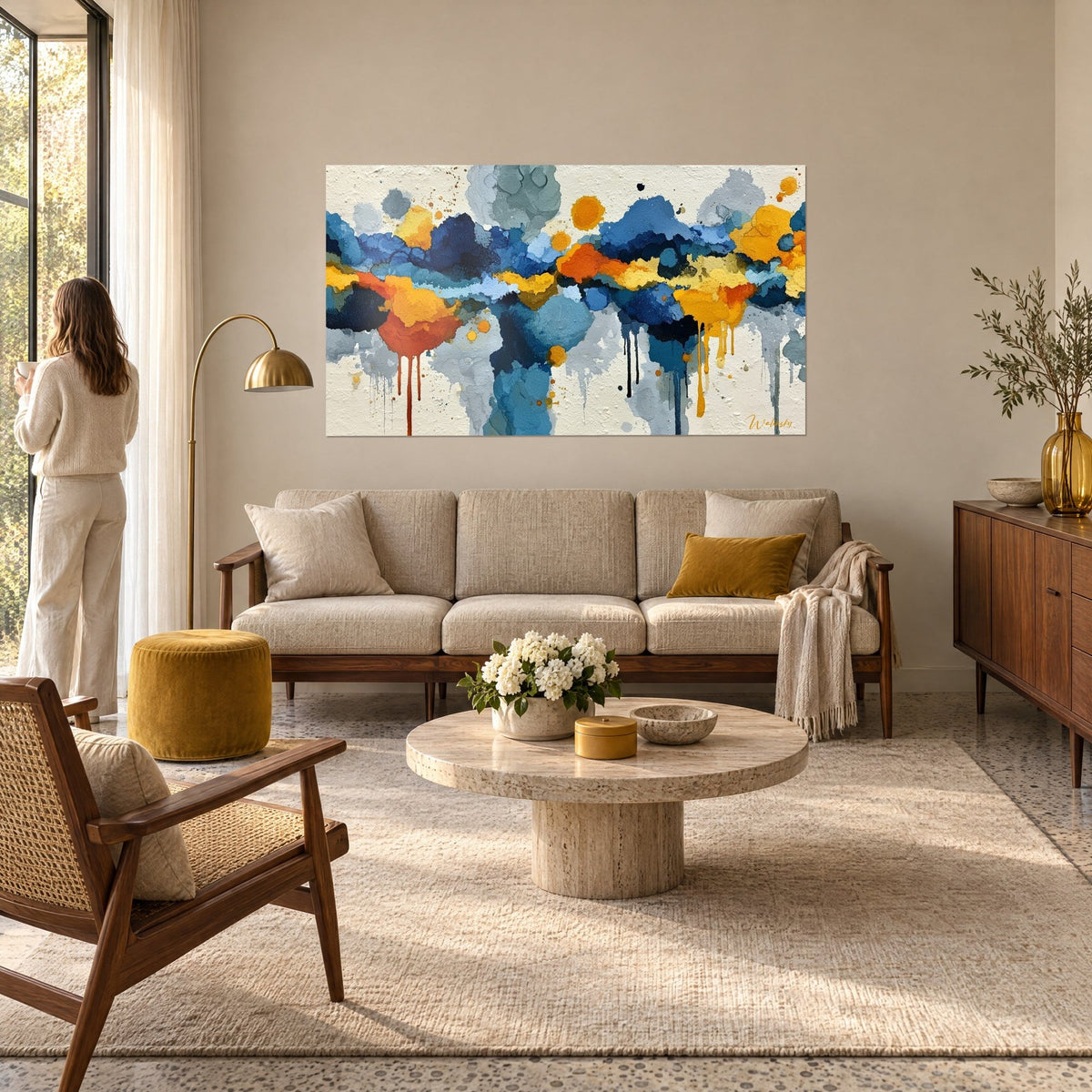 Schilderij met druipende marineblauwe en okerkleurige wolken, oranje druipsporen op crèmekleurige achtergrond, vrouw met de rug naar de kijker, boven een bank in een lichte woonkamer