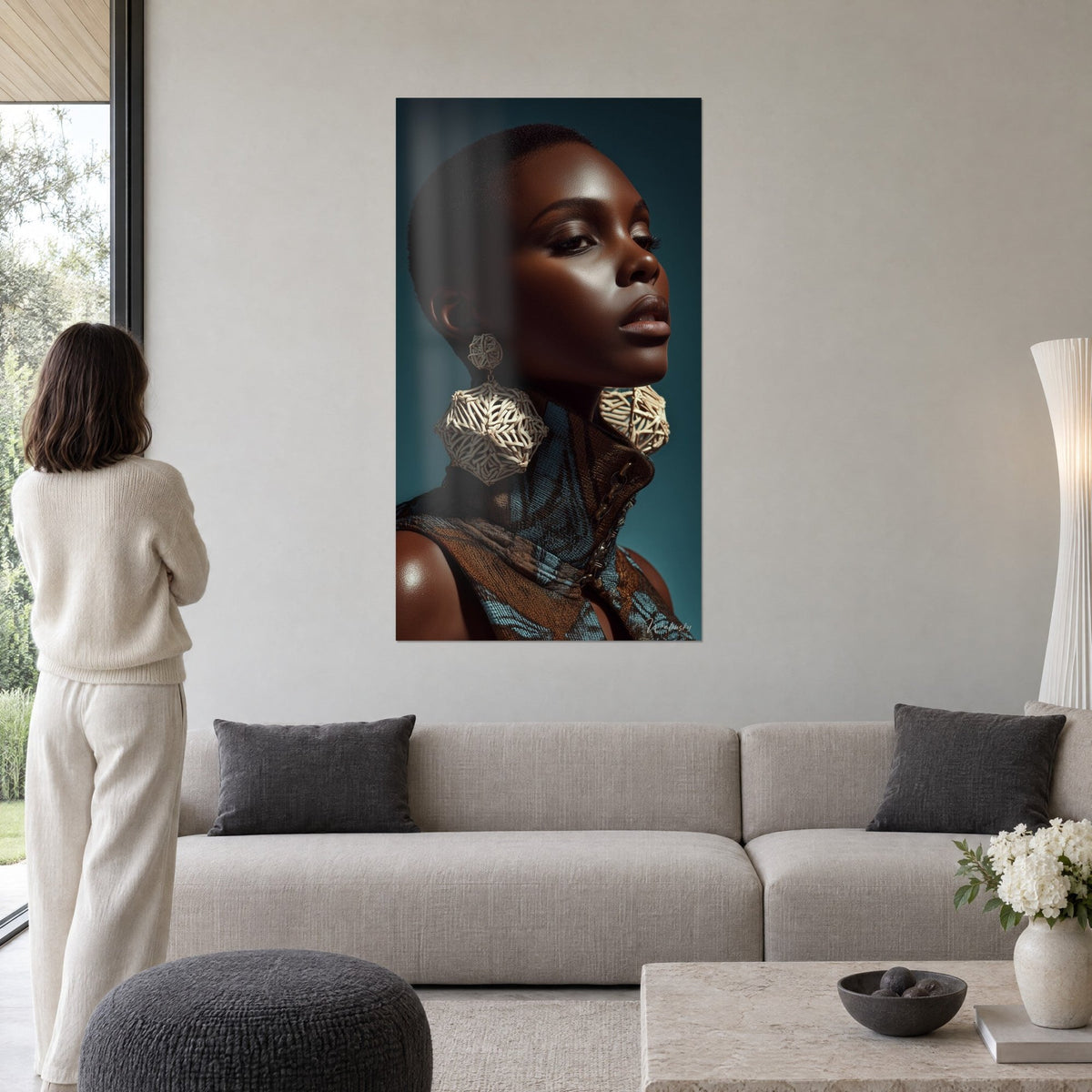 Tableau portrait de femme au crâne rasé, grosses boucles beige ajourées sur fond bleu canard, au-dessus d'un canapé dans un salon lumineux