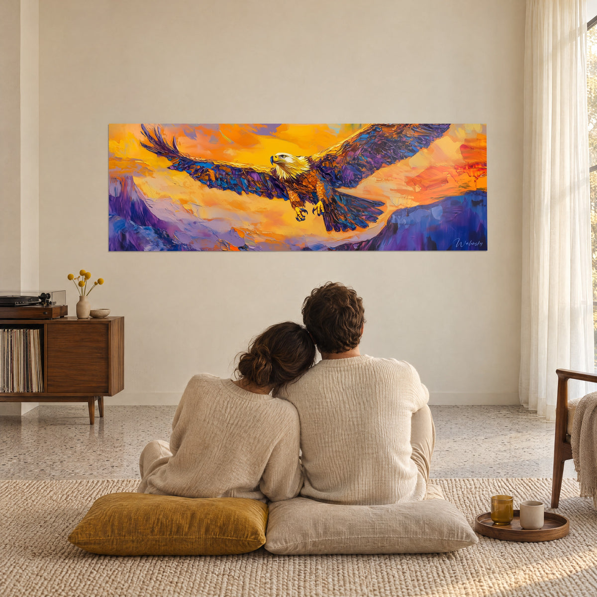 Cuadro majestuoso vuelo de un ave rapaz, alas púrpuras y cobrizas sobre fondo anaranjado, pareja de espaldas sentada sobre cojines