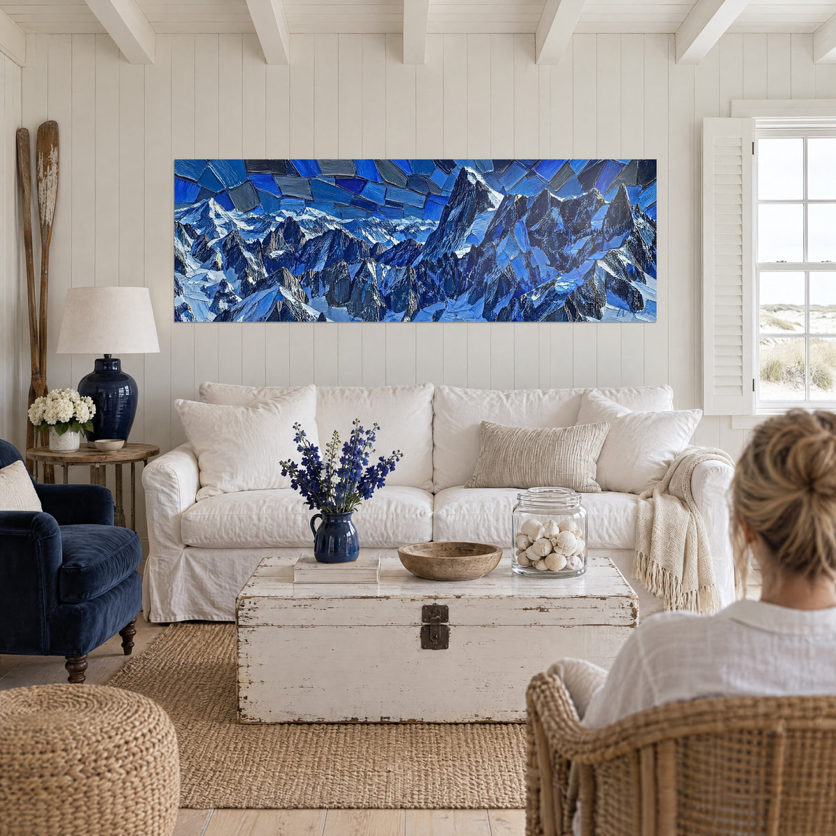 Tableau cimes alpines en pâte épaisse bleu nuit et blanc glacé, deux femmes de dos, au-dessus d'un canapé dans un salon lumineux