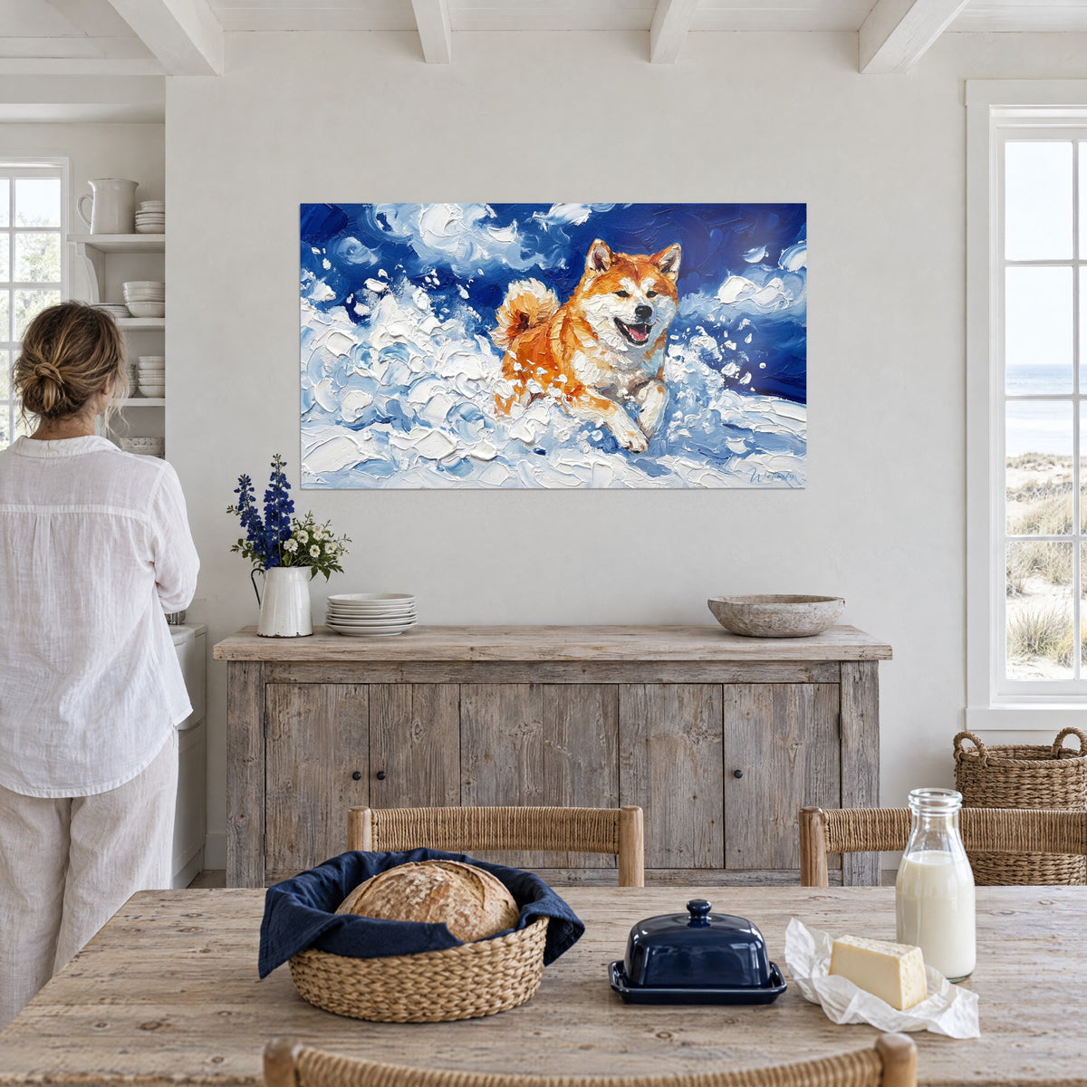 Gemälde orangefarbener Hund im Lauf durch himmelblau-weiße Schneeflocken, eine Frau von hinten vor einem Küchentisch am Meer