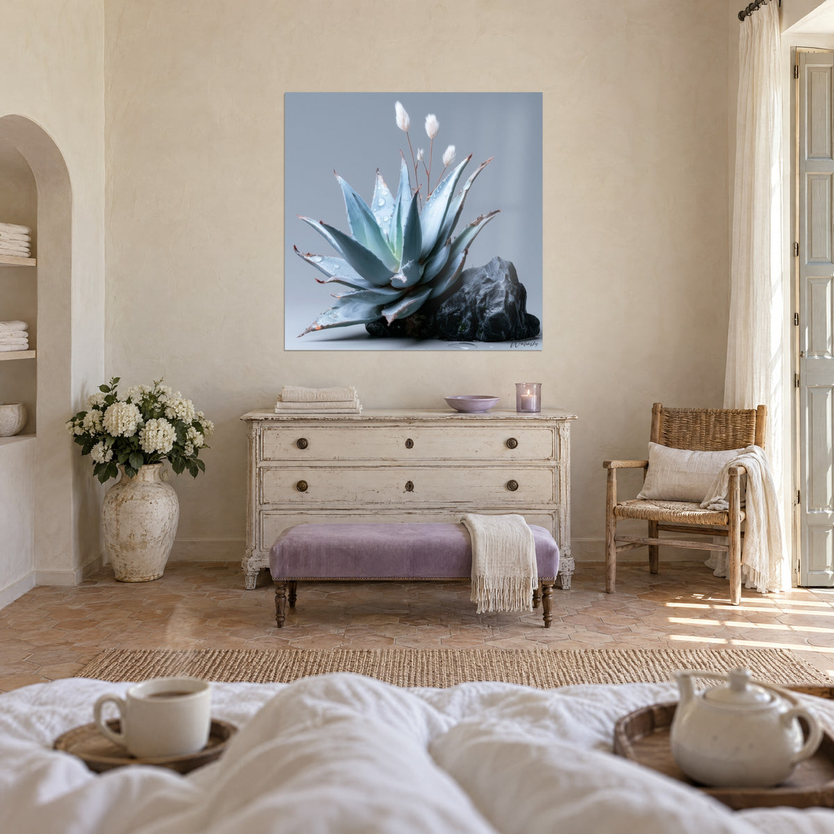 Tableau plante grasse gris-bleu et pierre sombre, perlée de rosée, sur un mur beige au-dessus d'un lit dans une chambre claire