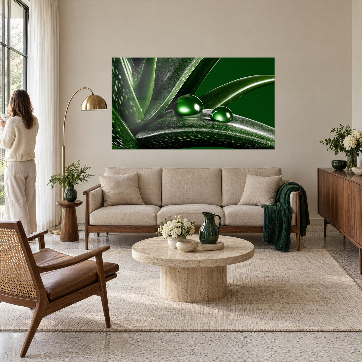 Wall art of an emerald green aloe leaf holding two shiny water droplets, woman seen from behind, above a sofa in a bright living room