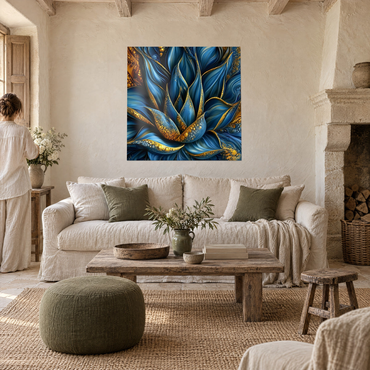 Tableau aloès bleu marine aux feuilles liserées d'or, une femme de dos le regarde, au-dessus d'un canapé dans un salon lumineux