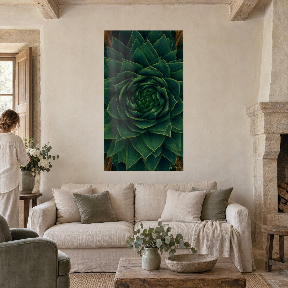 Wall art green aloe rosette with deep tones and rust-tipped points, a woman seen from behind above a sofa in a bright living room
