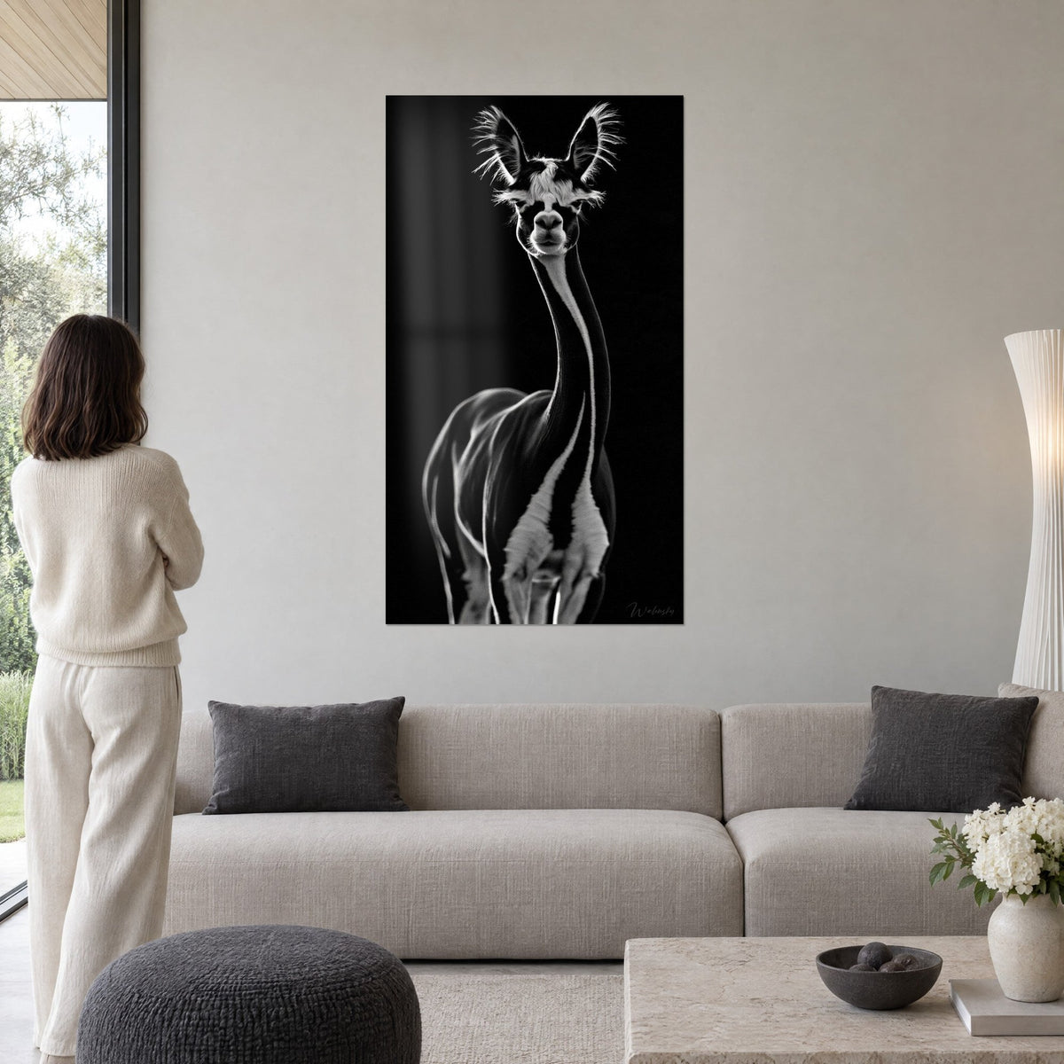 Tableau alpaga noir et argent au long cou, oreilles frangées de lumière, femme de dos, au-dessus d'un canapé dans un salon lumineux