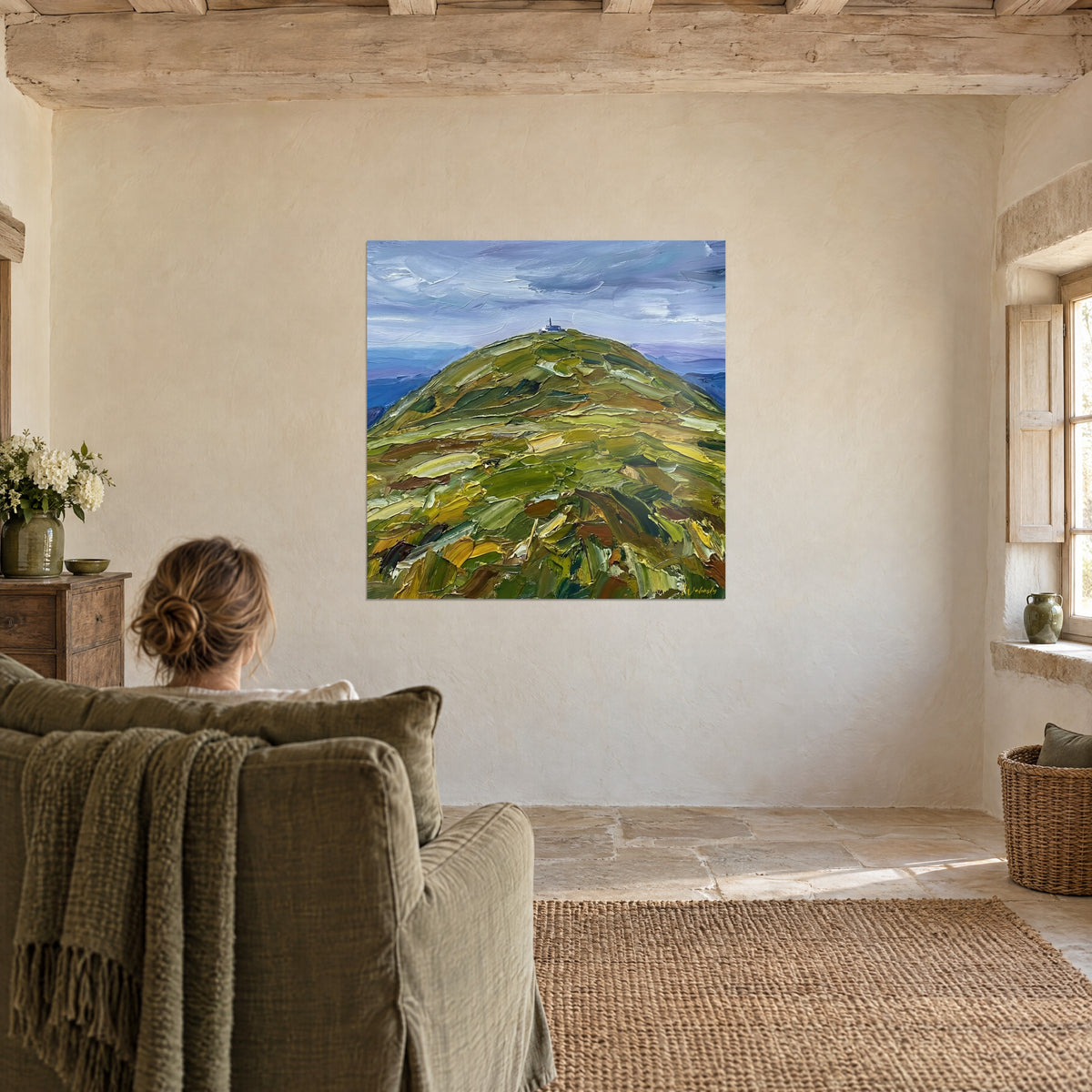 Quadro montagna strutturata in un monocromo di verdi e ocre sotto un cielo pastello, contemplata da una poltrona in una stanza essenziale
