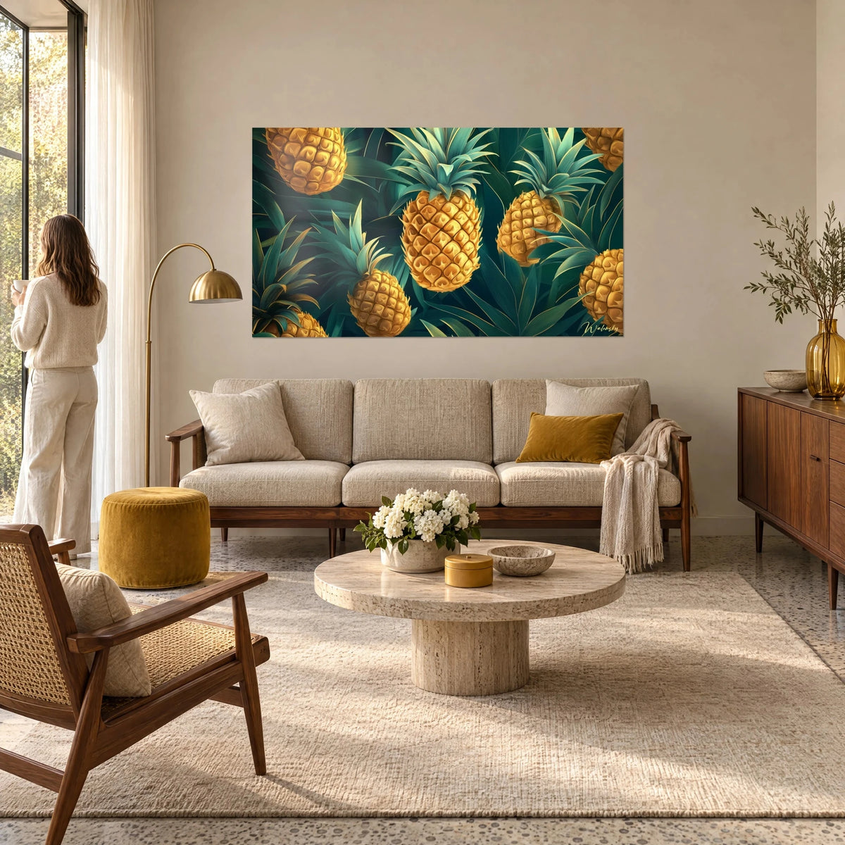 Quadro ananas dorati con foglie verde smeraldo su fondo scuro, una donna di spalle lo guarda sopra un divano in un soggiorno luminoso