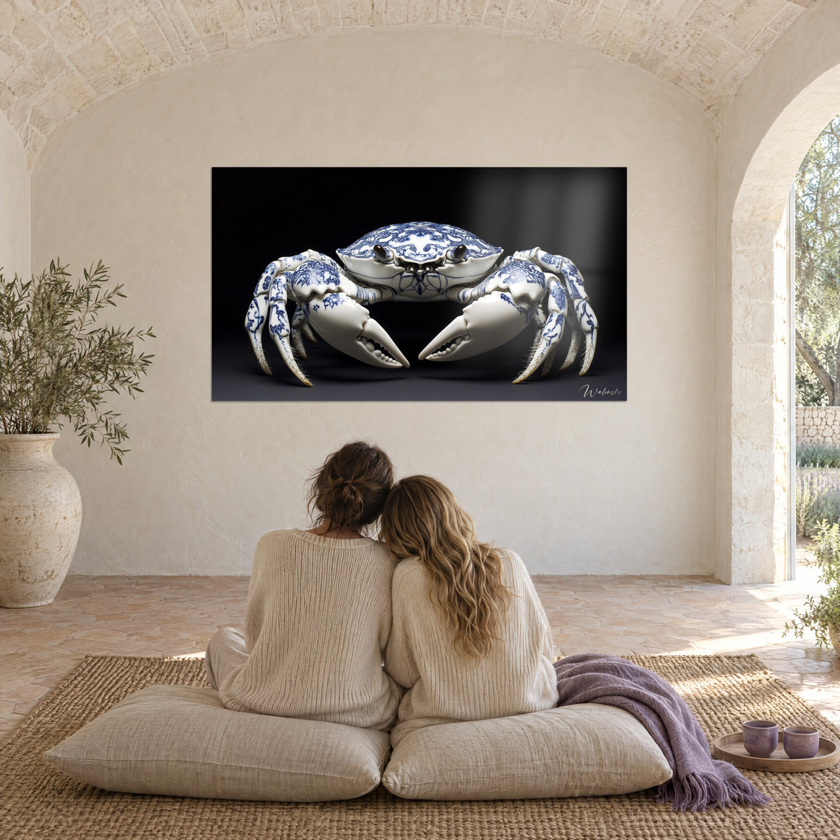 Cuadro cangrejo escultural de porcelana blanca veteada de azul real, fondo negro profundo, dos amigas abrazadas sobre cojines en una sala abovedada