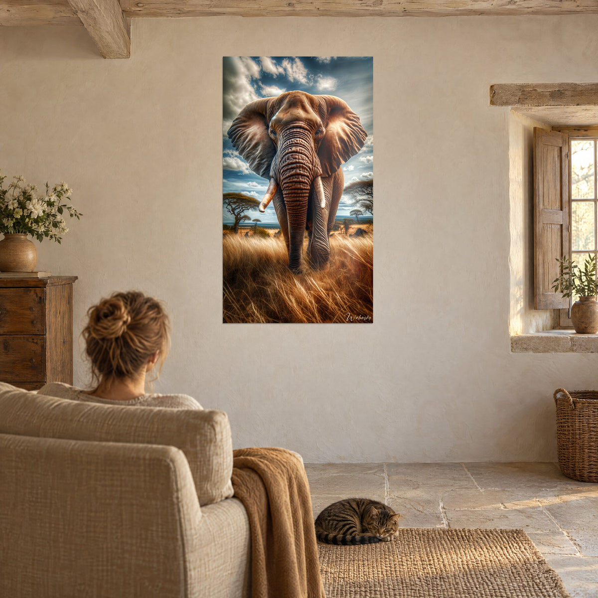 Schilderij van een majestueuze olifant die door het gouden gras loopt, stormachtige blauwe lucht, vrouw van achteren in een beige fauteuil, getijgerde kat