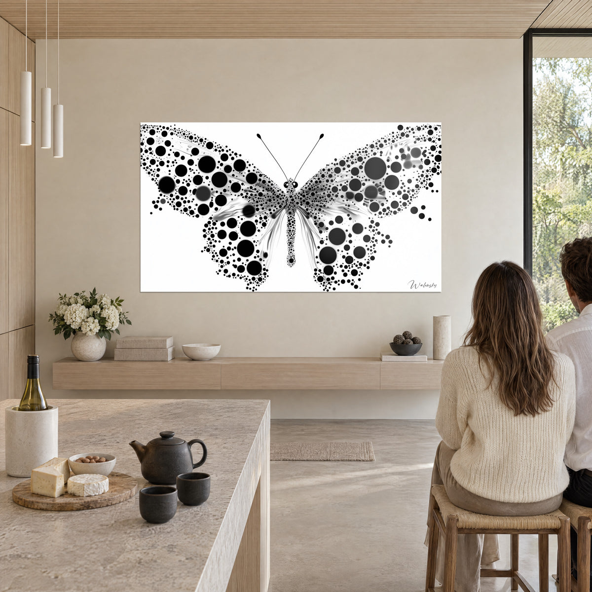 Cuadro alas de mariposa con grandes discos negros y micropuntos, fondo blanco, cocina abierta de madera clara y piedra beige