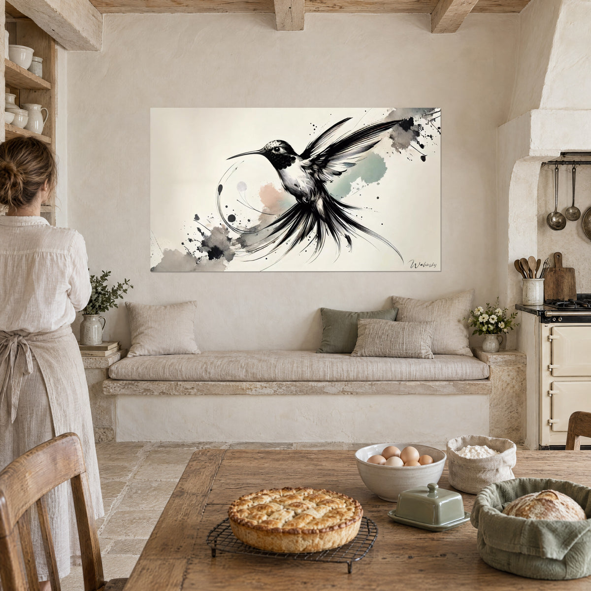 Wall art of a hummingbird silhouette drawn with a quill, black wing spread out on an ivory background, facing a woman in a rustic kitchen