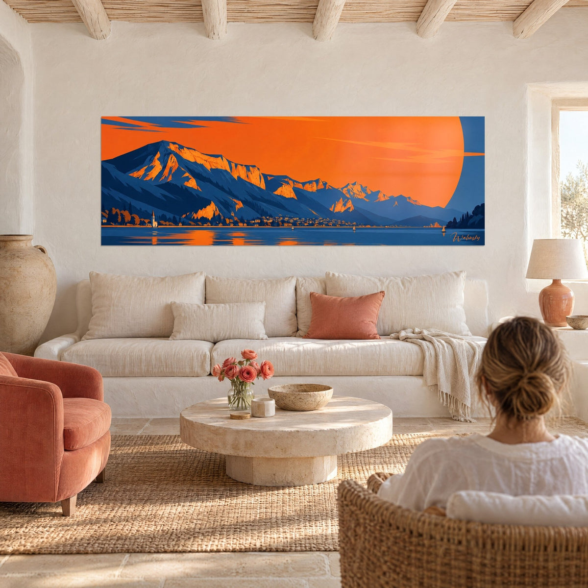 Wall art alpine panorama with a giant orange sun over blue peaks, shimmering lake, above a sofa in a bright living room