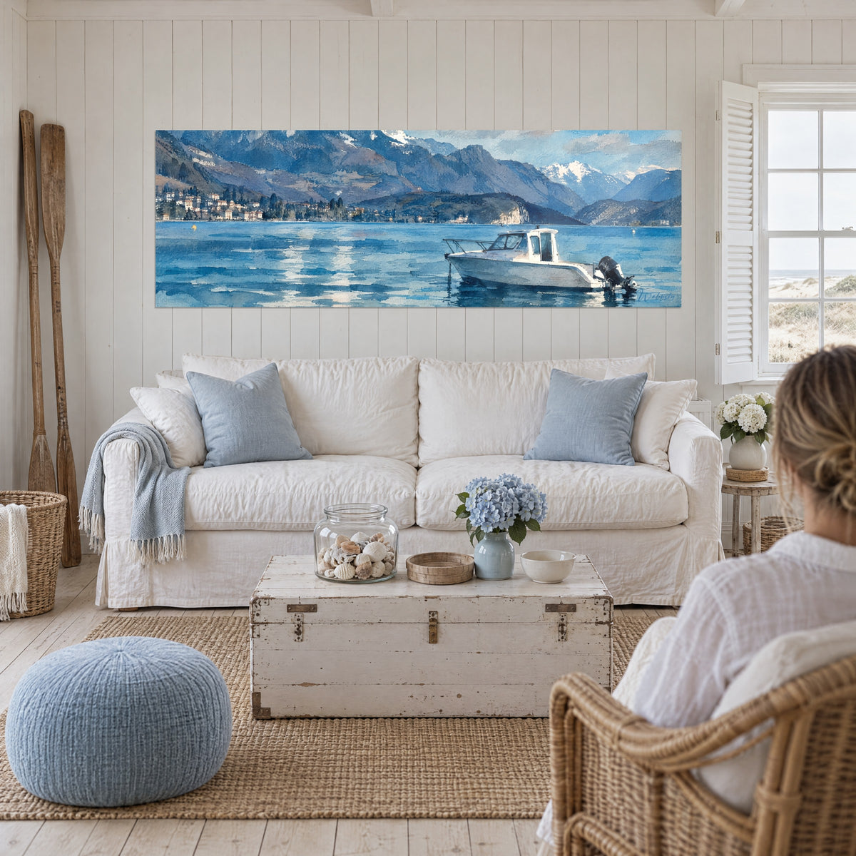 Gemälde eines weißen Motorboots auf einem türkisfarbenen See, graublaue Berge im Hintergrund, über einem Sofa in einem hellen Wohnzimmer