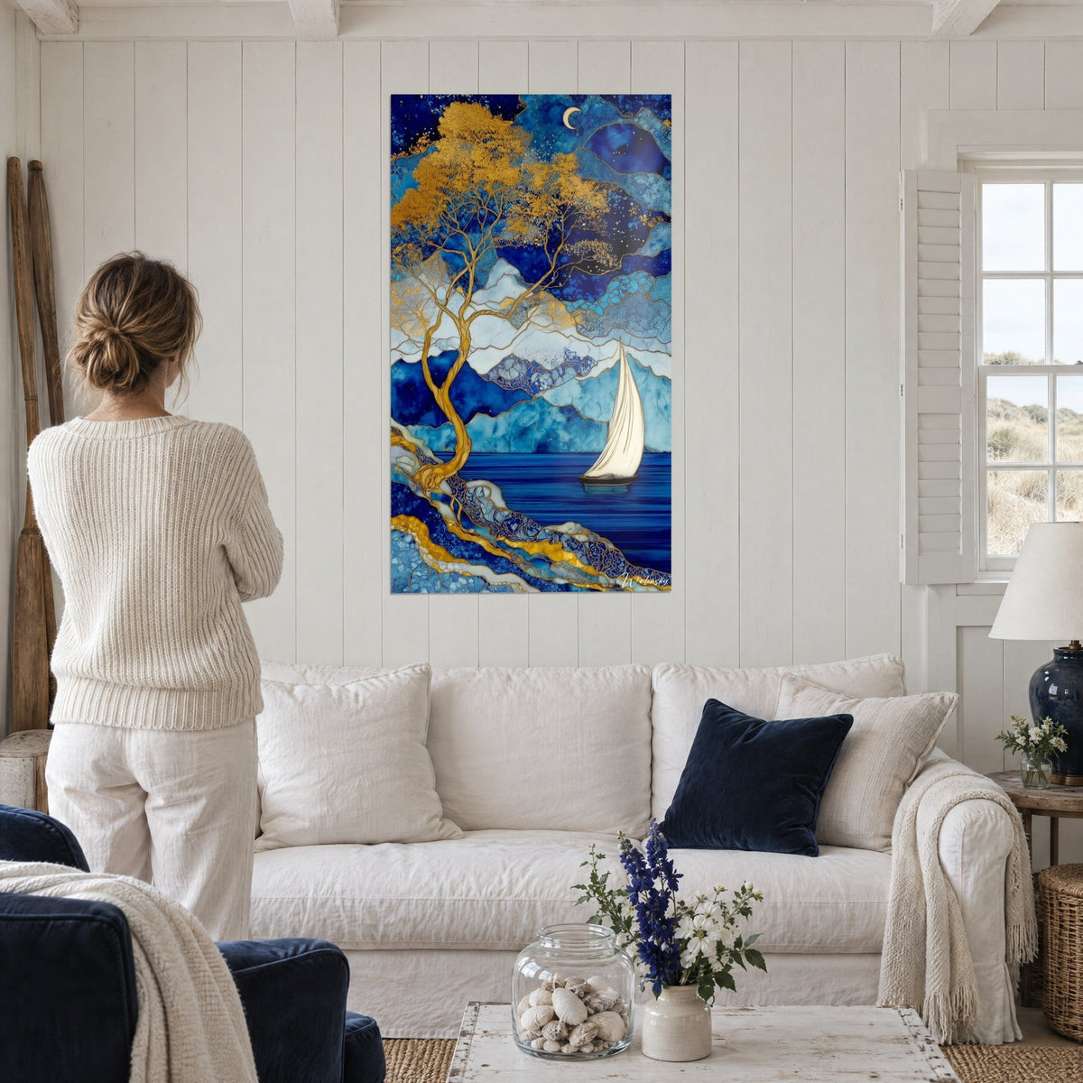 Tableau arbre aux feuilles d'or sur lac bleu, voilier ivoire et croissant de lune, au-dessus d'un canapé dans un salon lumineux