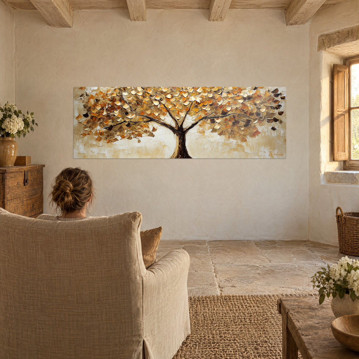 Cuadro árbol con ramaje ocre y dorado, numerosas hojas en pinceladas de espátula, frente a un sillón de lino en una casa de piedra