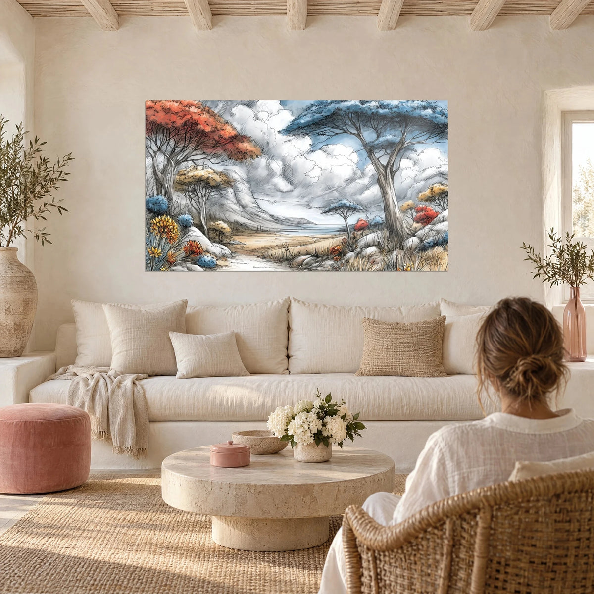 Wall art acacia trees with rust and slate-blue crowns under a cloudy sky, woman seen from behind, above a sofa in a bright living room