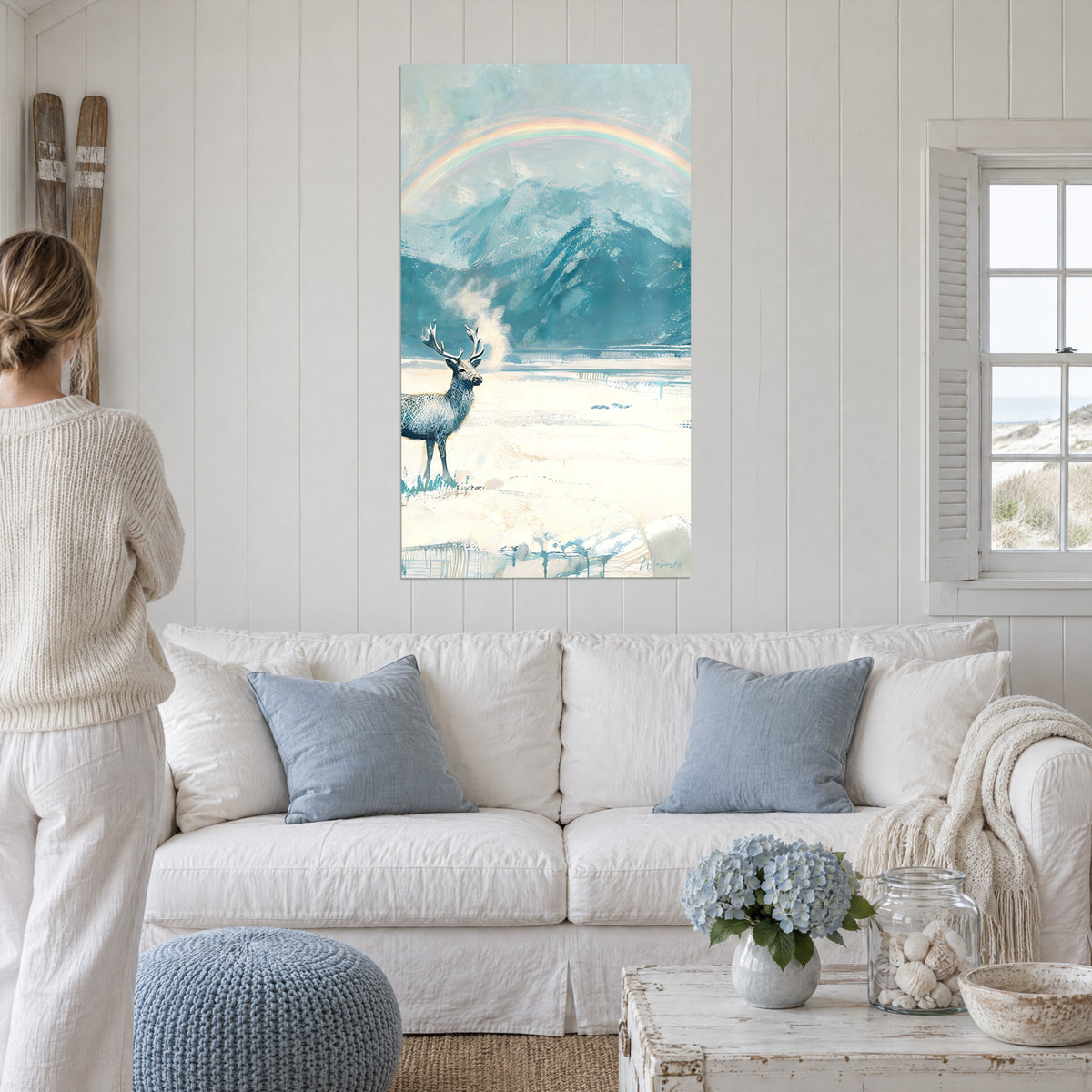 Wall art silver stag with a misty breath, pastel rainbow over blue mountains, above a sofa in a bright living room