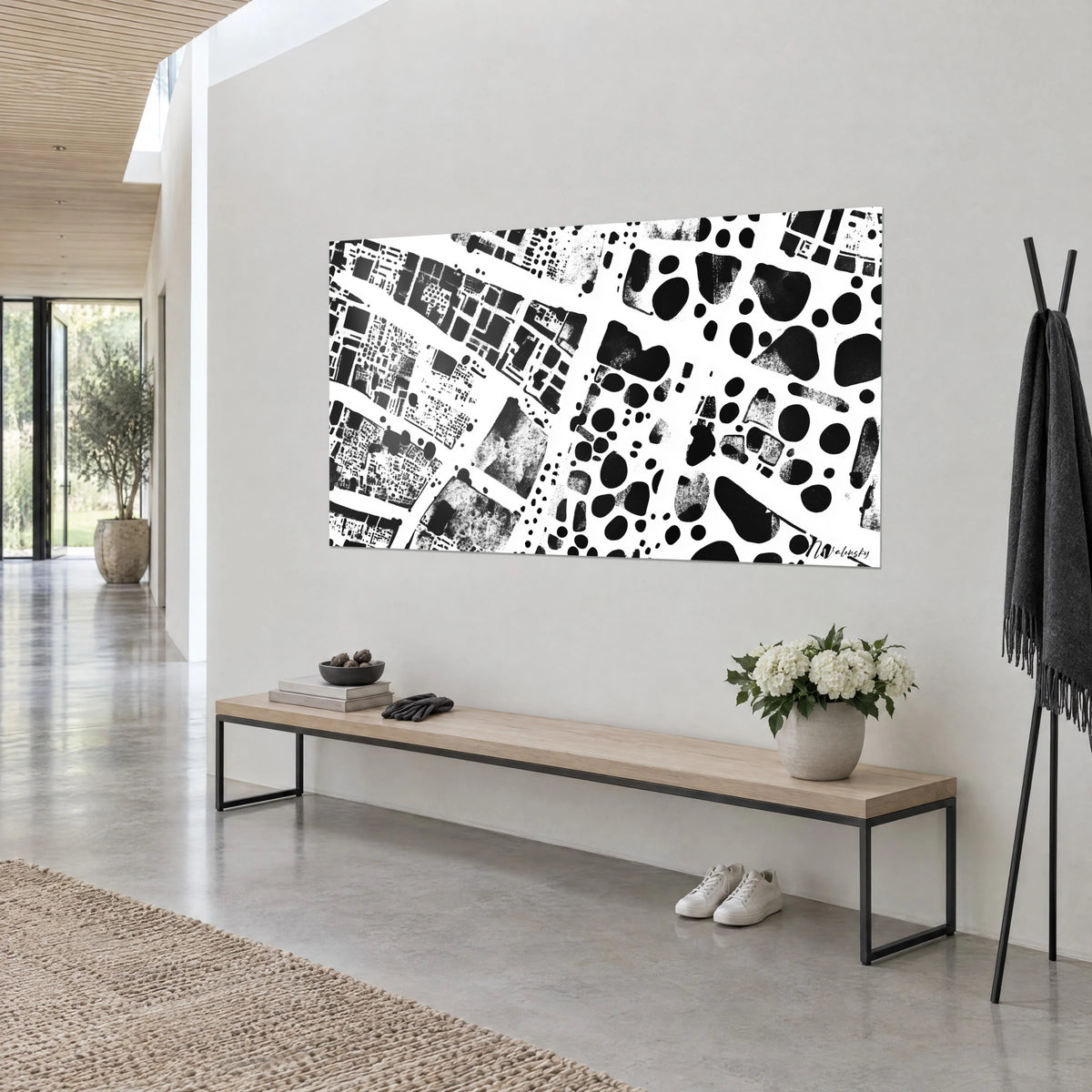 Tableau archipel d'îlots noirs éclaboussés, avenues blanches et blocs mouchetés, accroché sur un mur gris clair au-dessus d'un banc en bois
