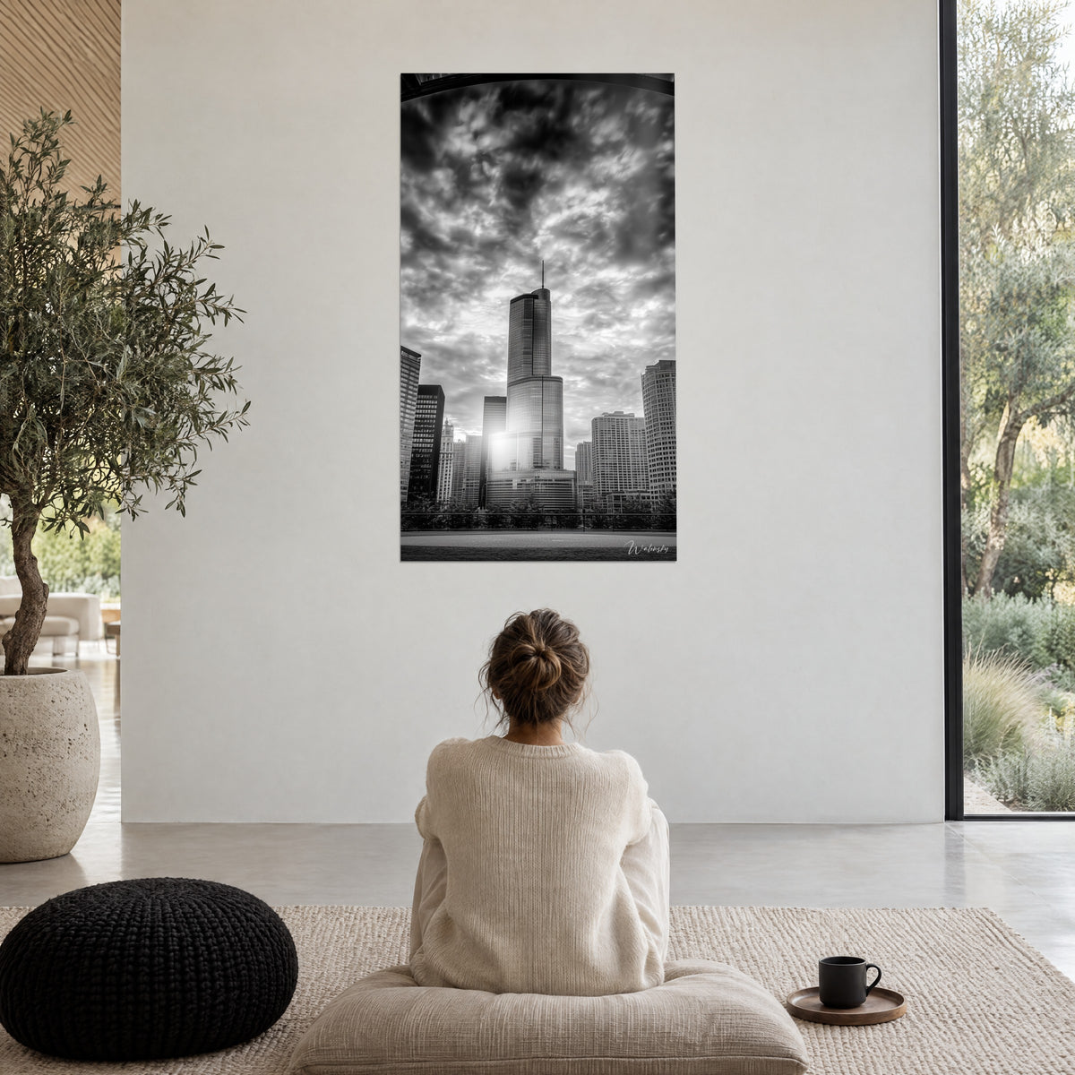 Wall art of a skyscraper in black and white, heavy dark grey and white sky, woman seen from behind on a cushion, black cup placed beside her