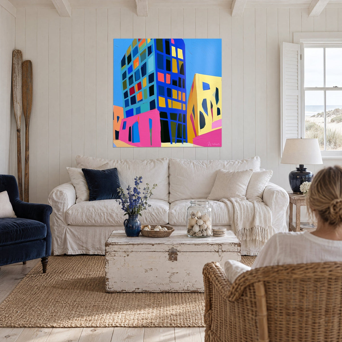 Tableau immeuble bleu cobalt aux fenêtres jaunes et orange, façade rose au pied, au-dessus d'un canapé dans un salon lumineux