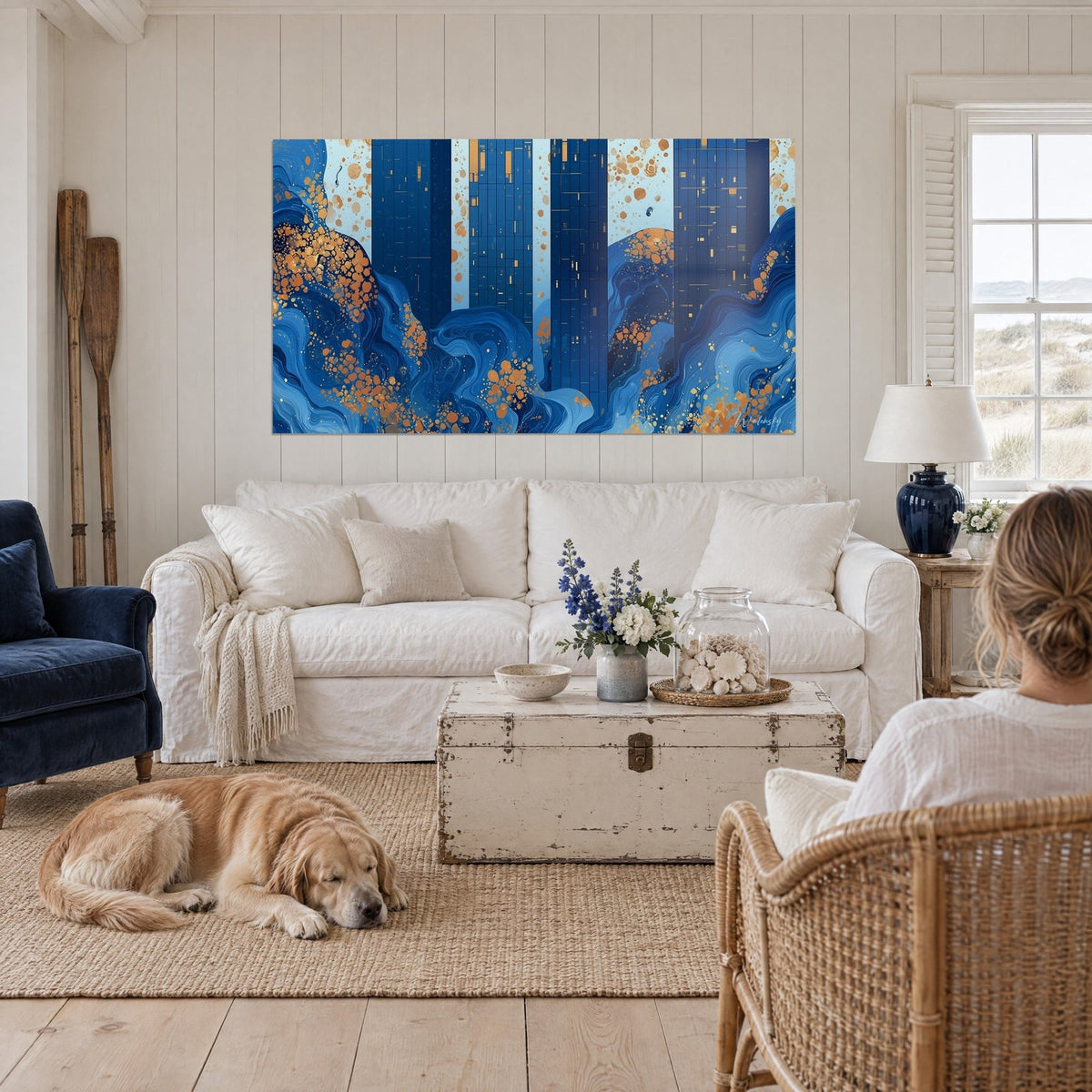 Tableau gratte-ciel indigo piqués d'éclats cuivrés, vagues bleues au pied, une femme et un retriever, au-dessus d'un canapé dans un salon lumineux
