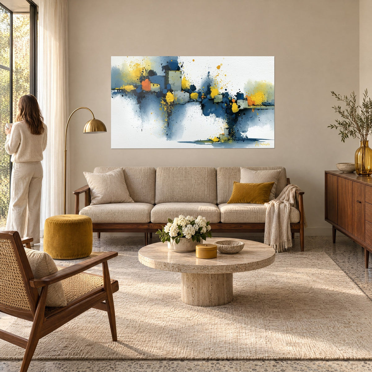 Tableau village abstrait aux cubes bleu marine et éclaboussures jaunes, une femme de dos, au-dessus d'un canapé dans un salon lumineux