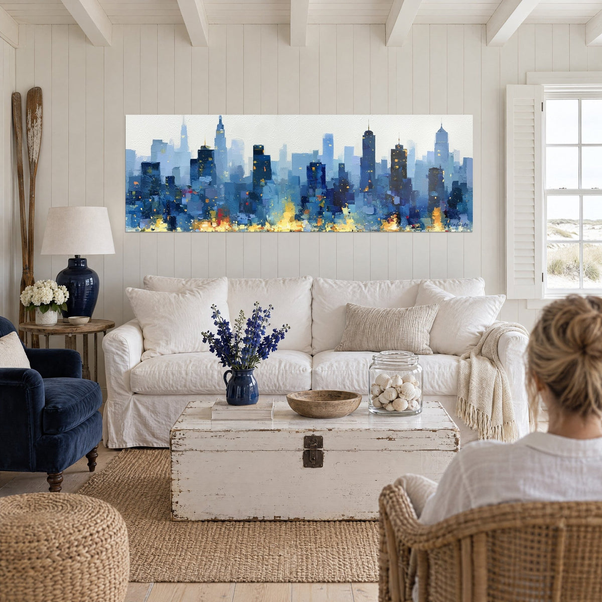 Tableau gratte-ciel bleu nuit aux fenêtres dorées, deux personnes de dos, au-dessus d'un canapé dans un salon lumineux