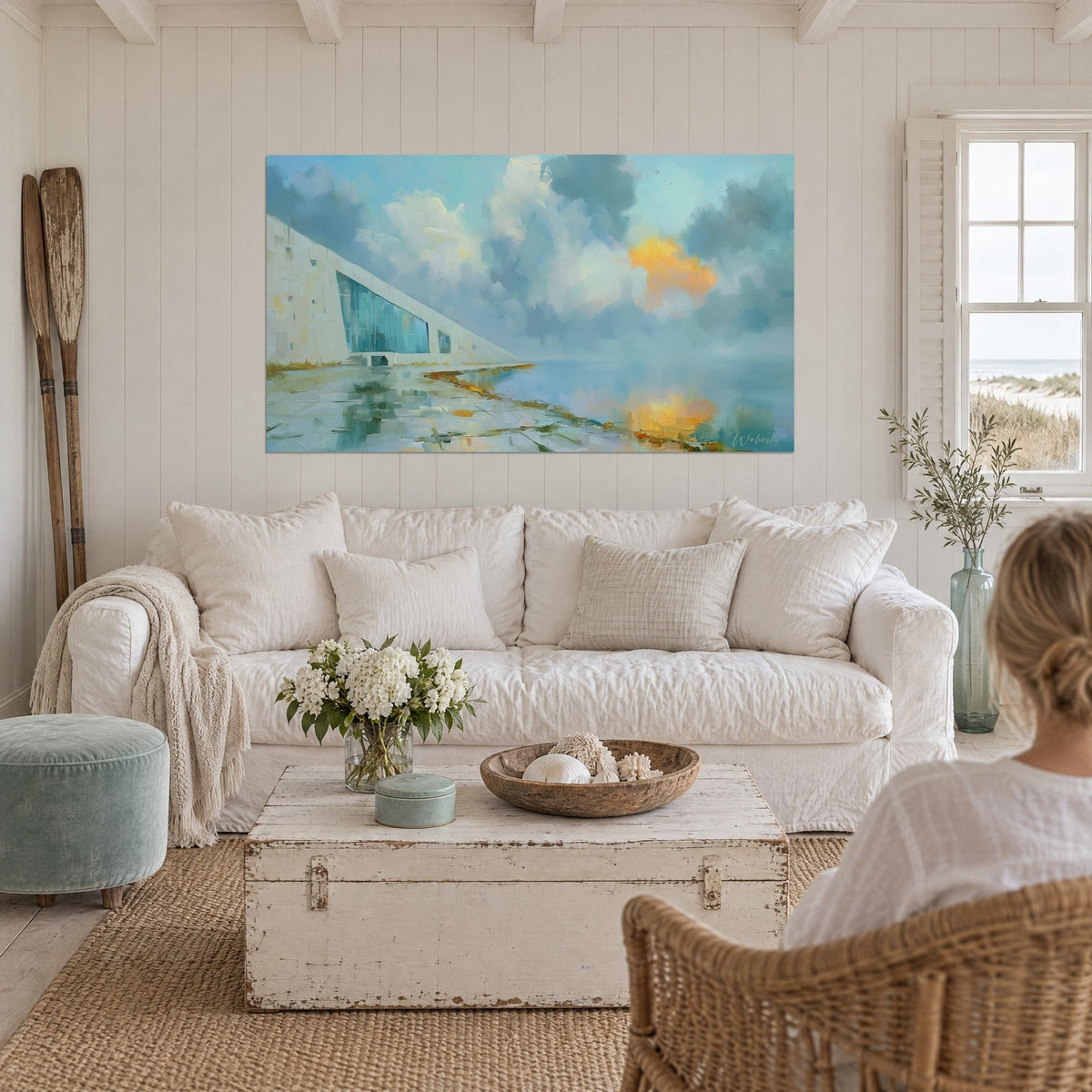 Wall art white triangular building with turquoise windows, blue and orange clouds, above a sofa in a bright living room