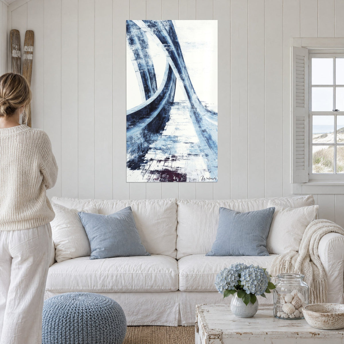 Tableau passerelle courbe aux coups de pinceau bleu nuit et blanc, femme de dos, au-dessus d'un canapé dans un salon lumineux