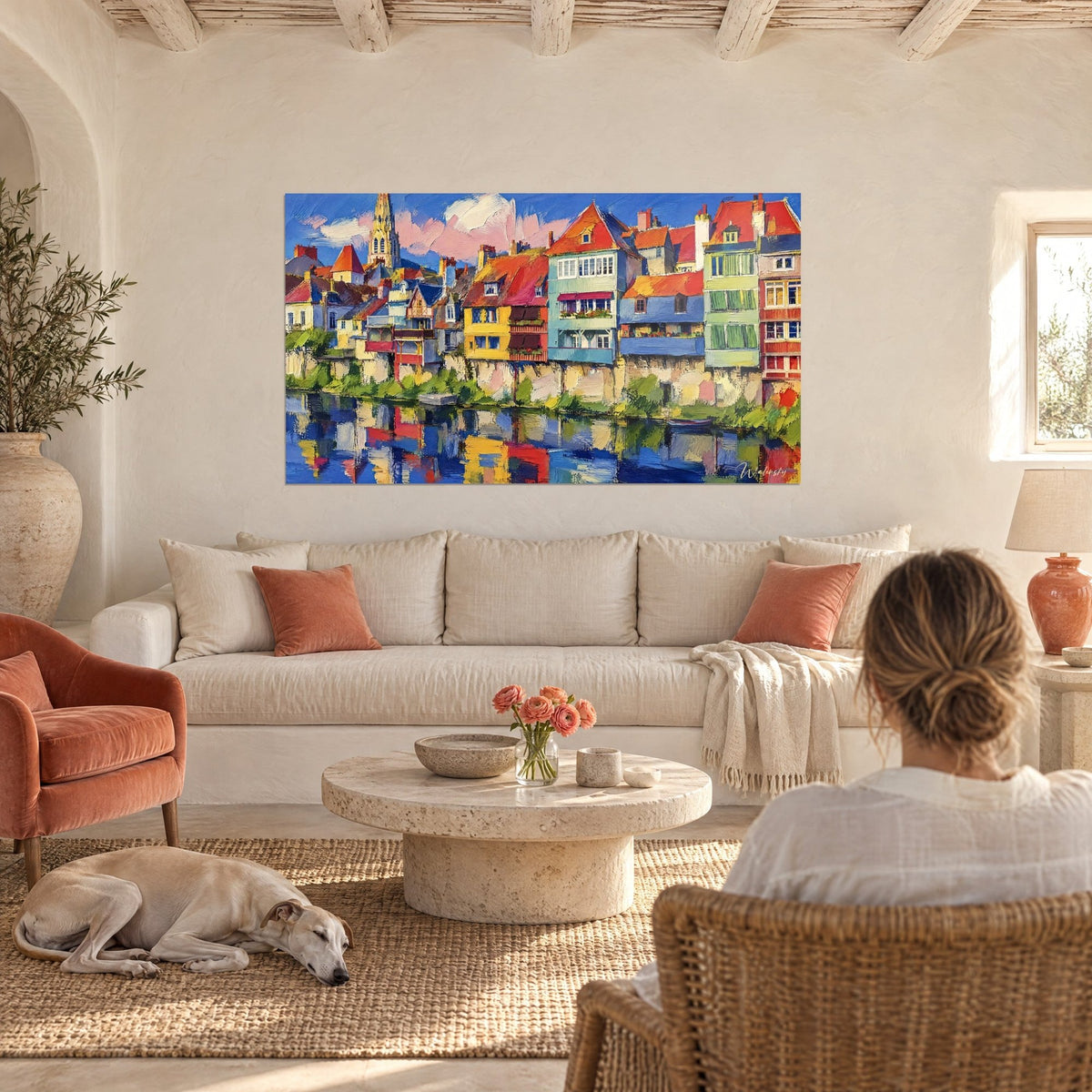 Wall art river village with bright red roofs and saffron-yellow facades, reflections in the water, reclining greyhound, above a sofa in a bright living room