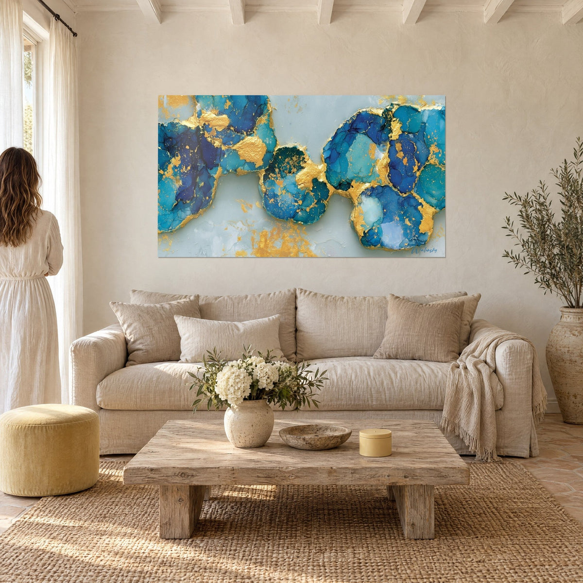 Tableau lagune minérale aux plaques turquoise cernées d'or, une femme de dos au-dessus d'un canapé dans un salon lumineux