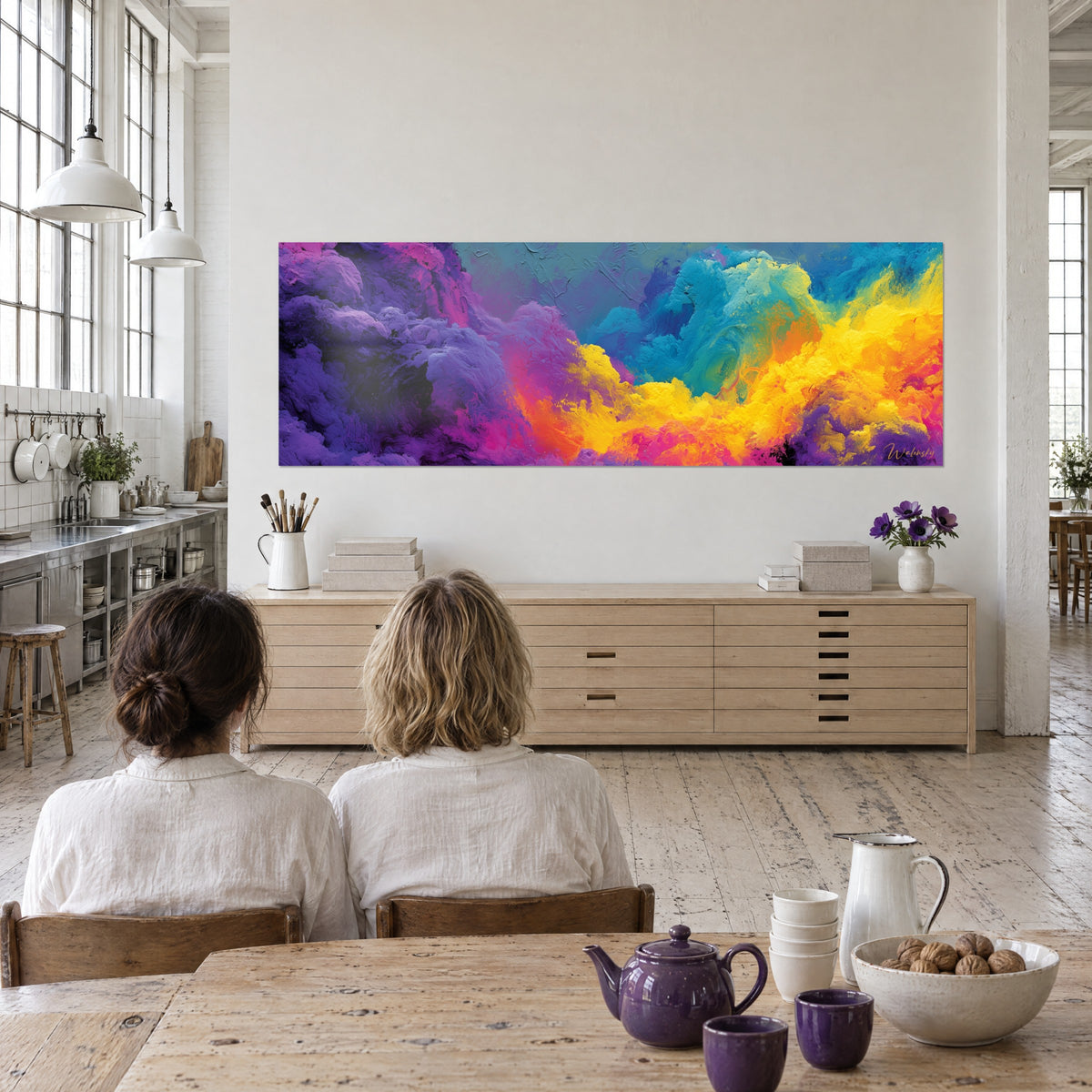 Quadro con un vortice di pittura densa gialla, rosa e blu, ammirato di spalle da due persone in una cucina di loft d'artista