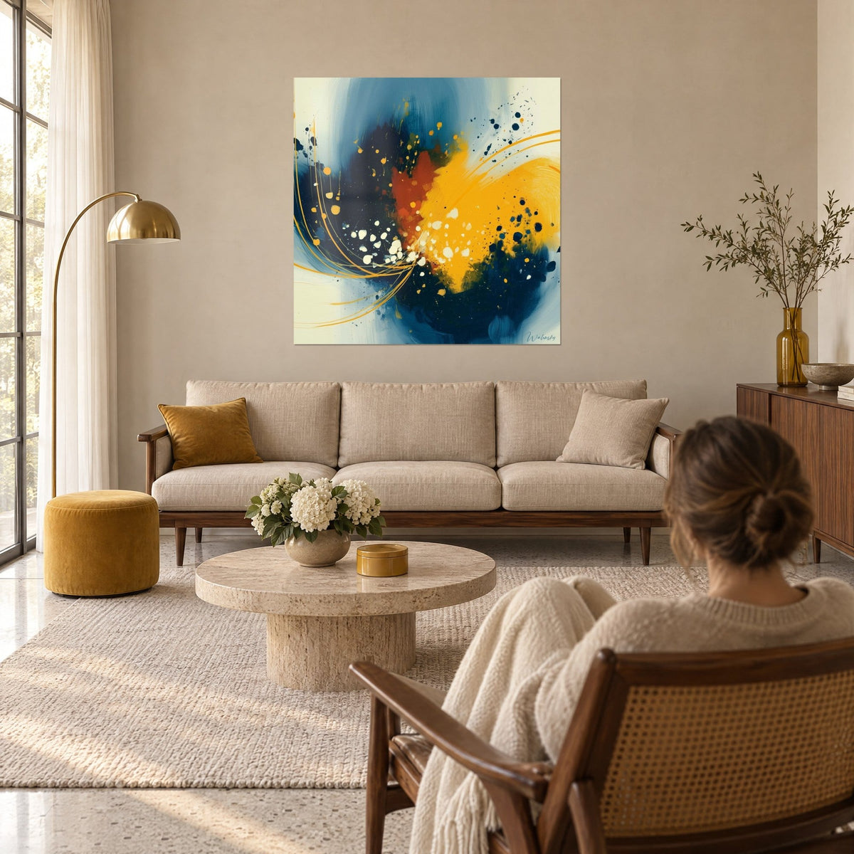 Tableau éclaboussures dorées sur bleu marine, tache rouille au centre, femme de dos, au-dessus d'un canapé dans un salon lumineux