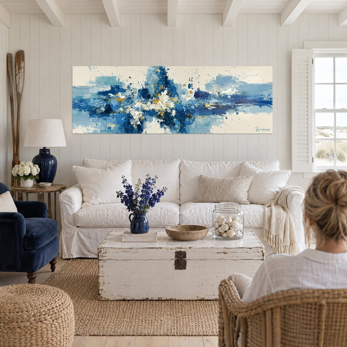 Tableau éclaboussure bleu marine et dorée sur fond crème, deux femmes de dos, au-dessus d'un canapé dans un salon lumineux