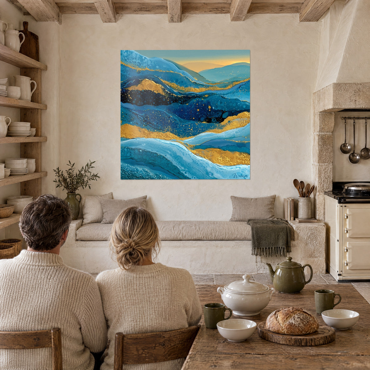Quadro paesaggio fluido con strati blu petrolio e sabbia dorata, coppia di spalle seduta a tavola vicino a una cucina rustica in pietra