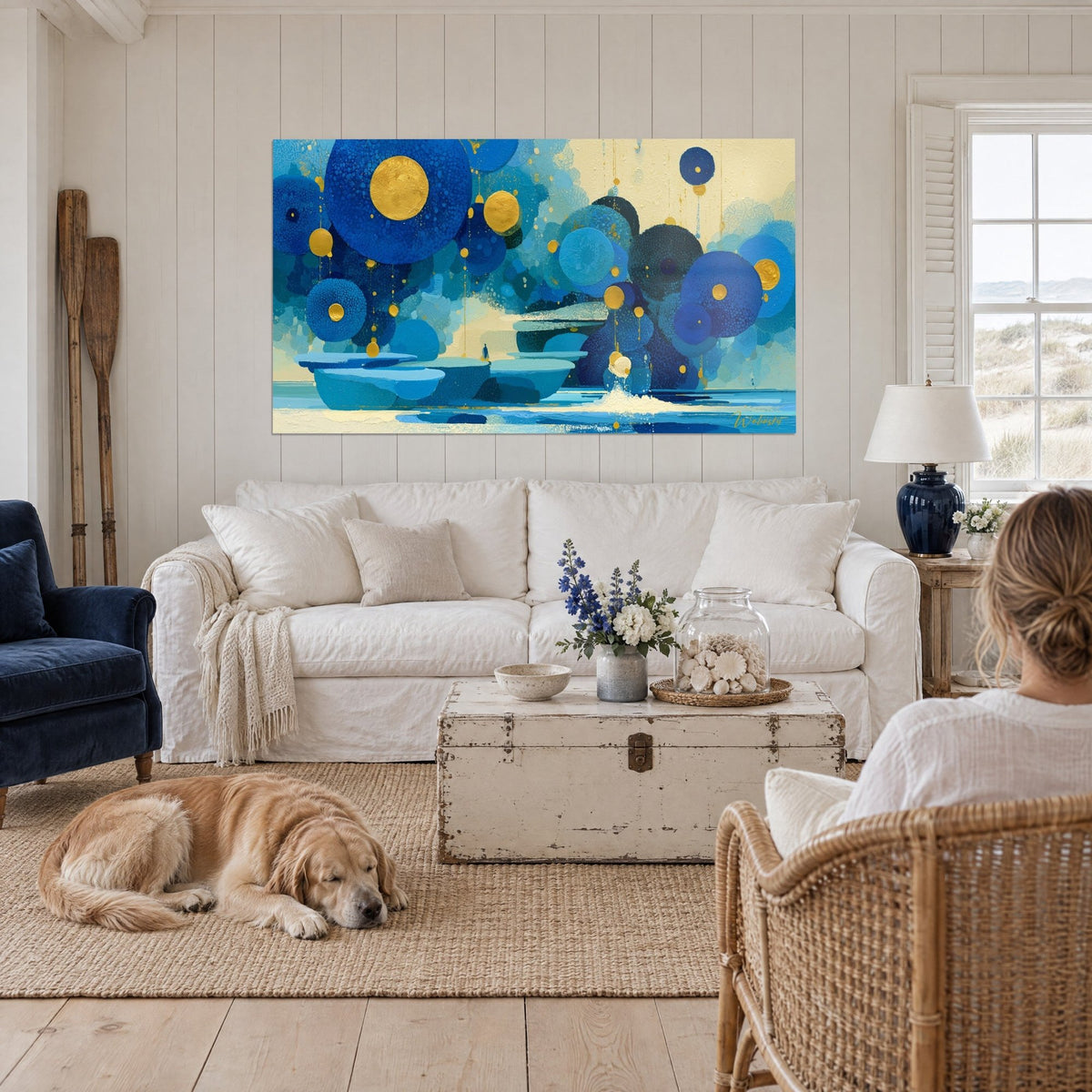 Tableau cercles bleu cobalt et or flottant sur une mer turquoise, deux silhouettes de dos et un retriever, au-dessus d'un canapé dans un salon lumineux